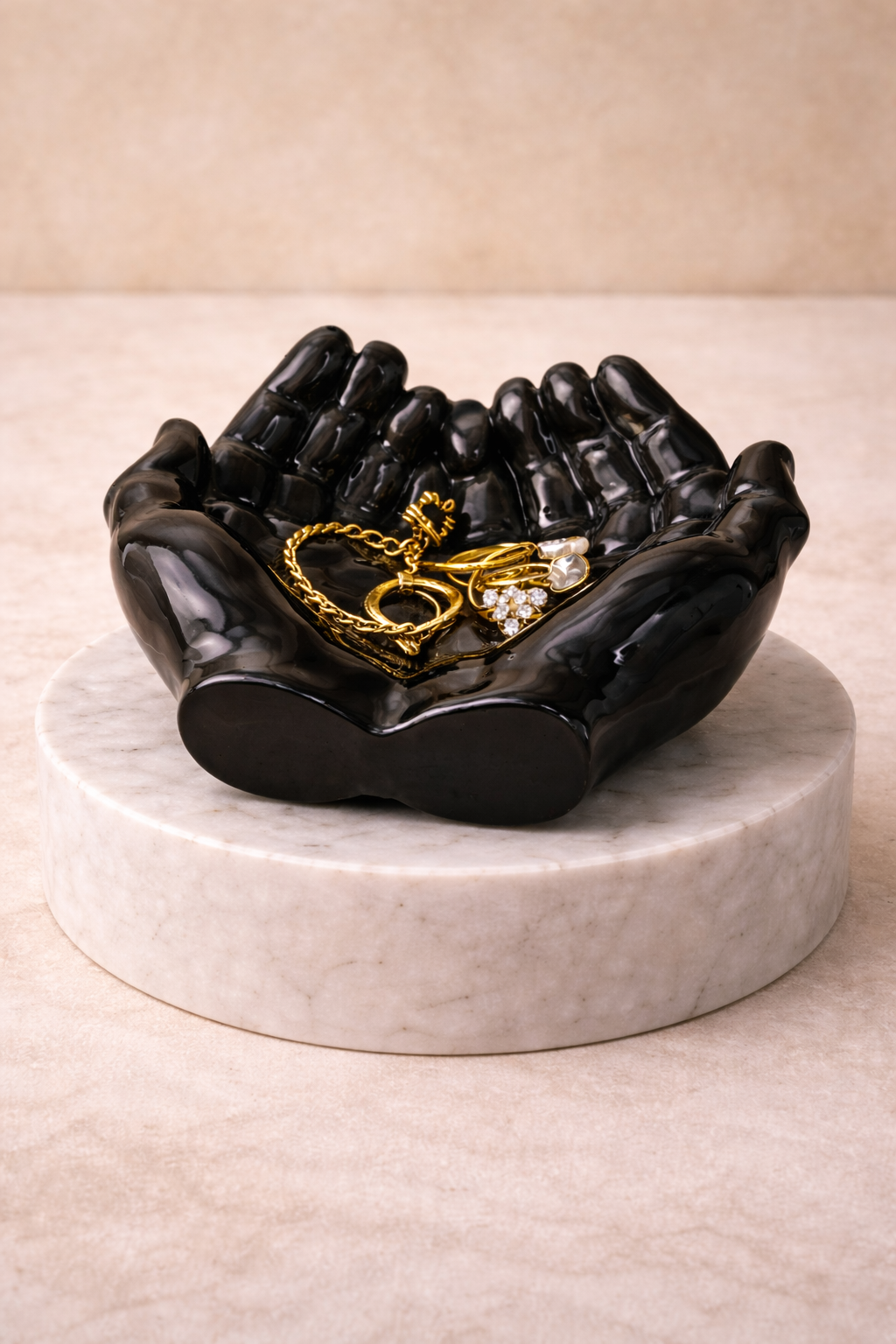 Black hand trinket dish jewelry holder on marble pedestal holding gold jewelry
