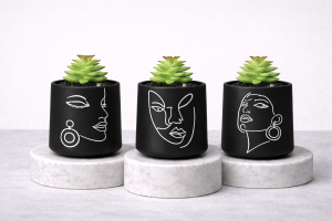 Matte black succulent jar trio with white abstract face line art on marble pedestals