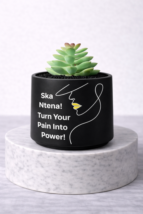 Matte black mini succulent jar with line art face design and the message “Ska Ntena! Turn Your Pain Into Power!” displayed on a white marble pedestal against a clean light grey background.