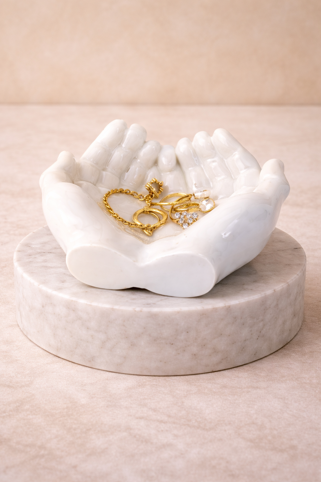 White hand trinket dish jewelry holder on marble pedestal holding gold jewelry